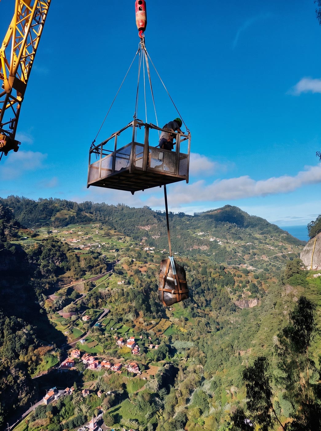 Bloco rochoso suspenso por grua em cesto de trabalho sobre vale da Madeira